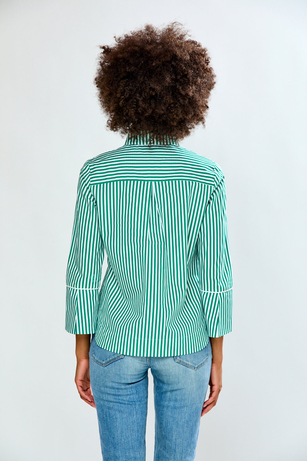 Person wearing a green and white striped shirt and blue jeans on a plain background