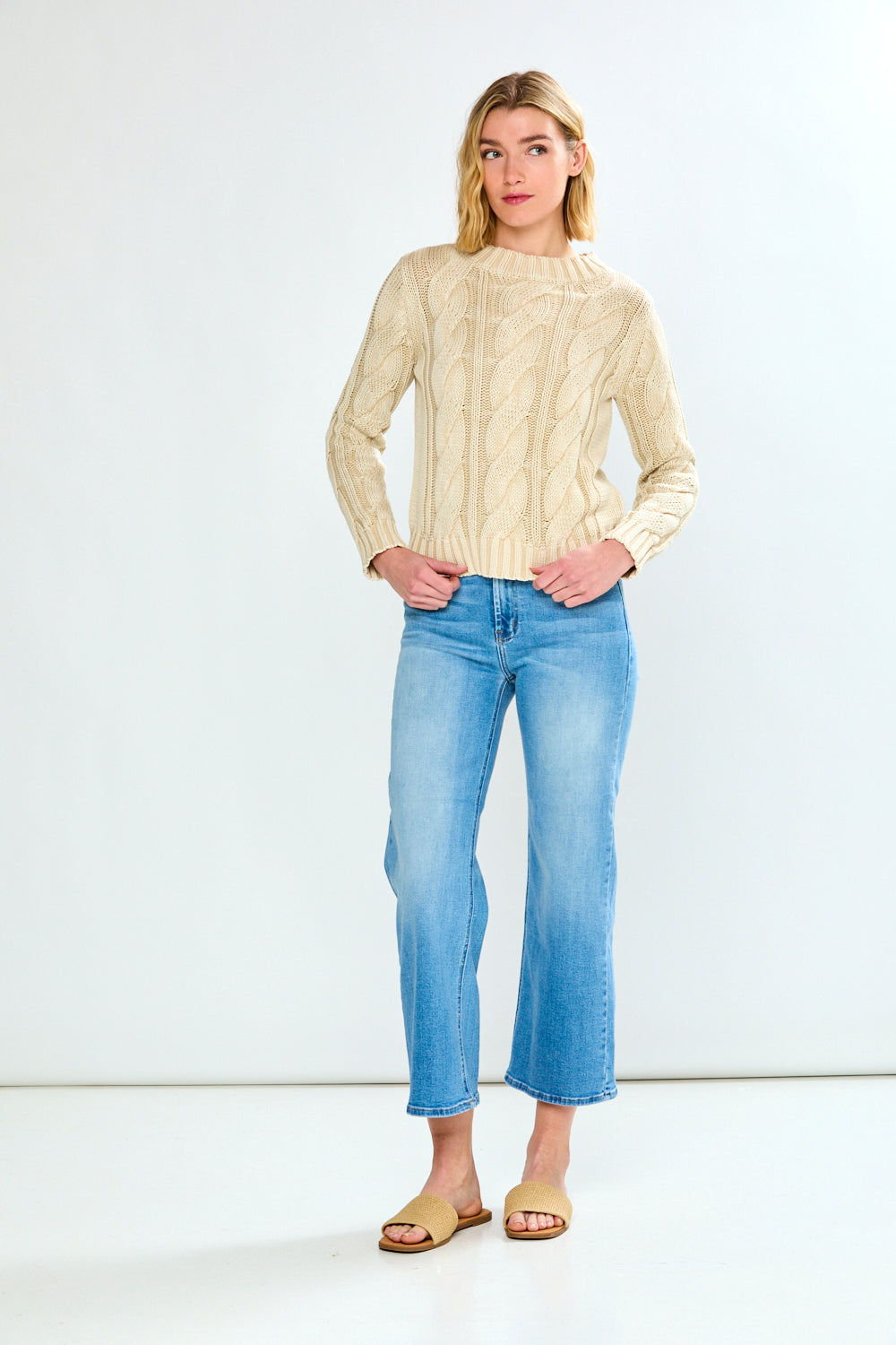 Woman wearing a pebble cable knit sweater and blue jeans on a white background