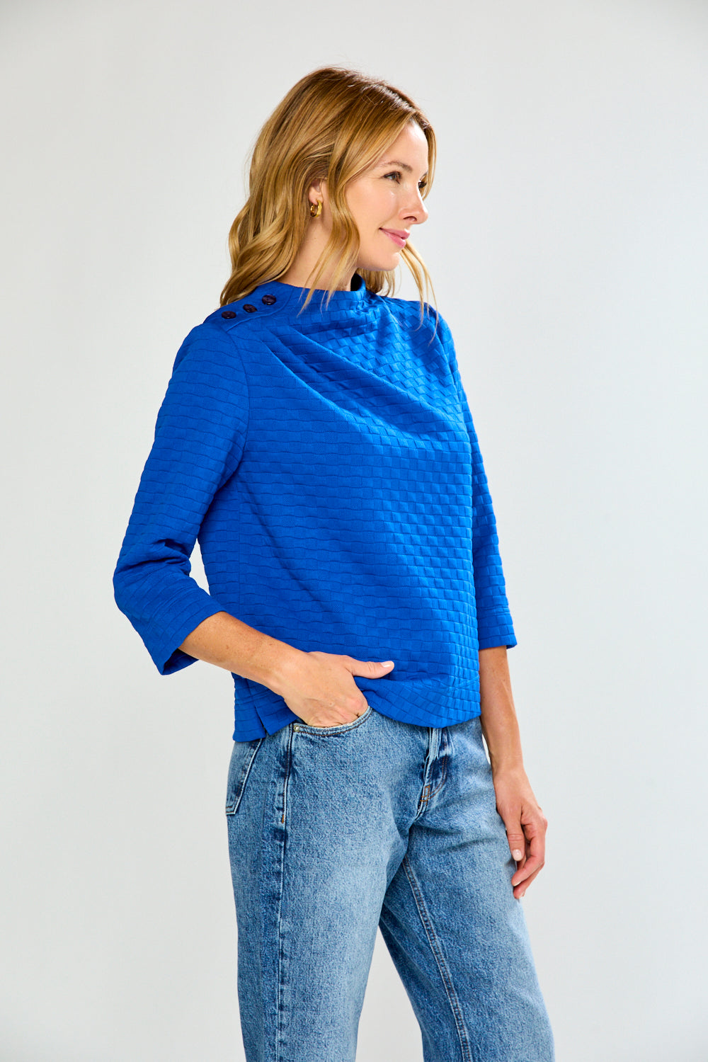 Woman wearing a blue textured top and jeans on a white background