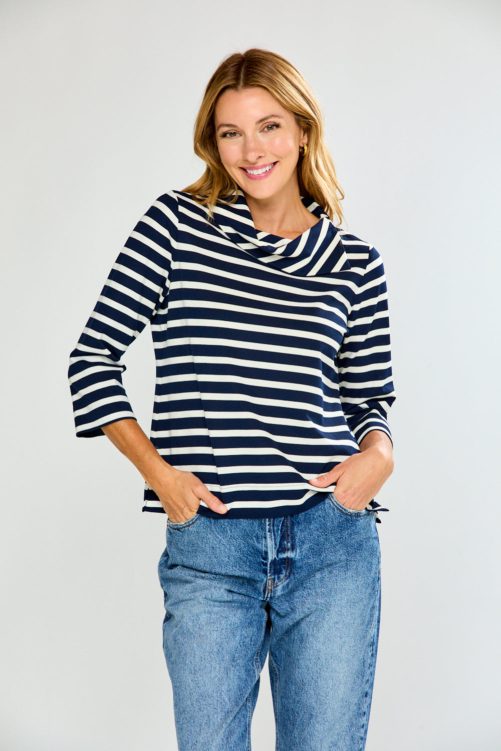 Woman wearing a navy and white striped sweater and blue jeans on a light gray background