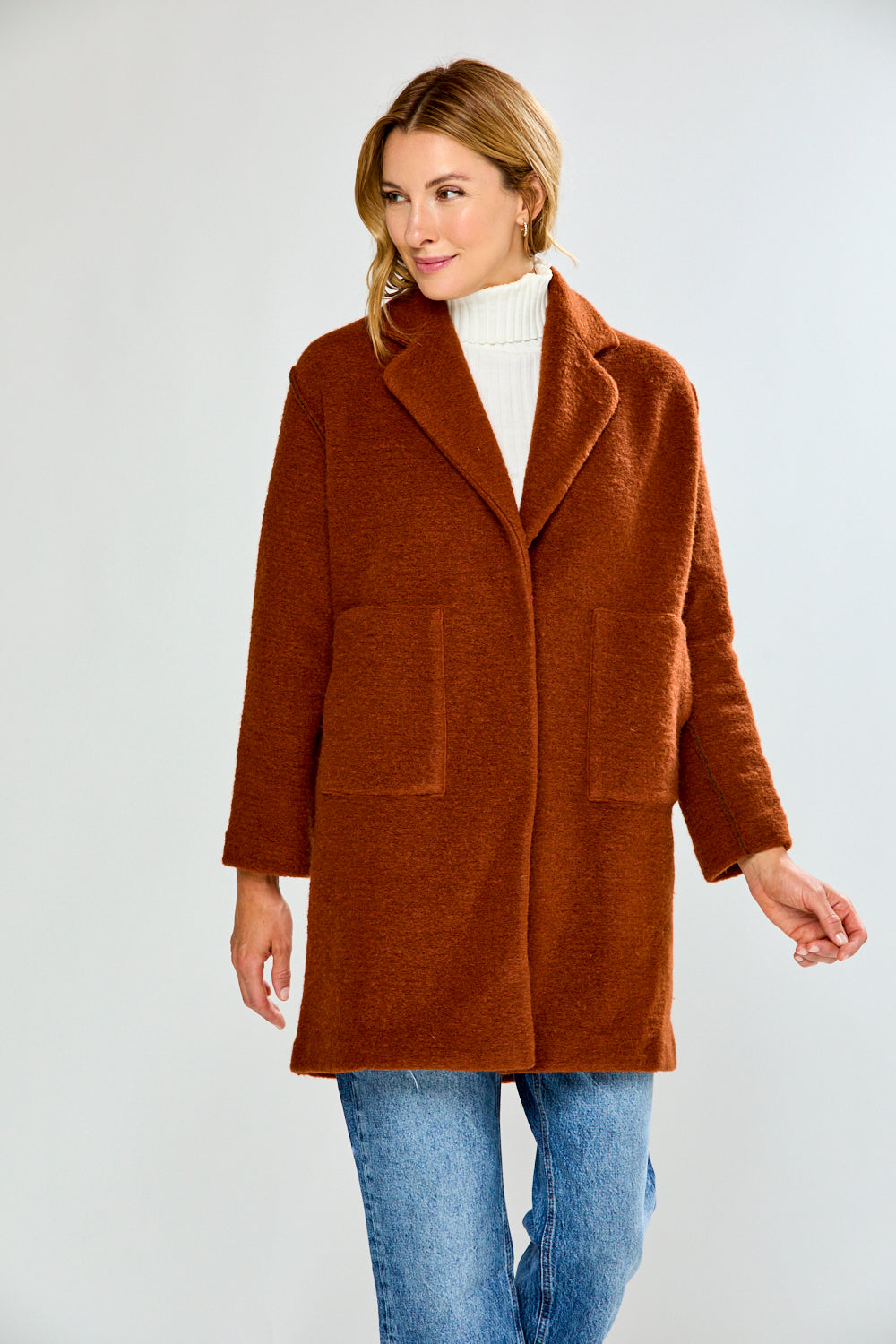 Woman wearing a brown coat over a white turtleneck on a white background
