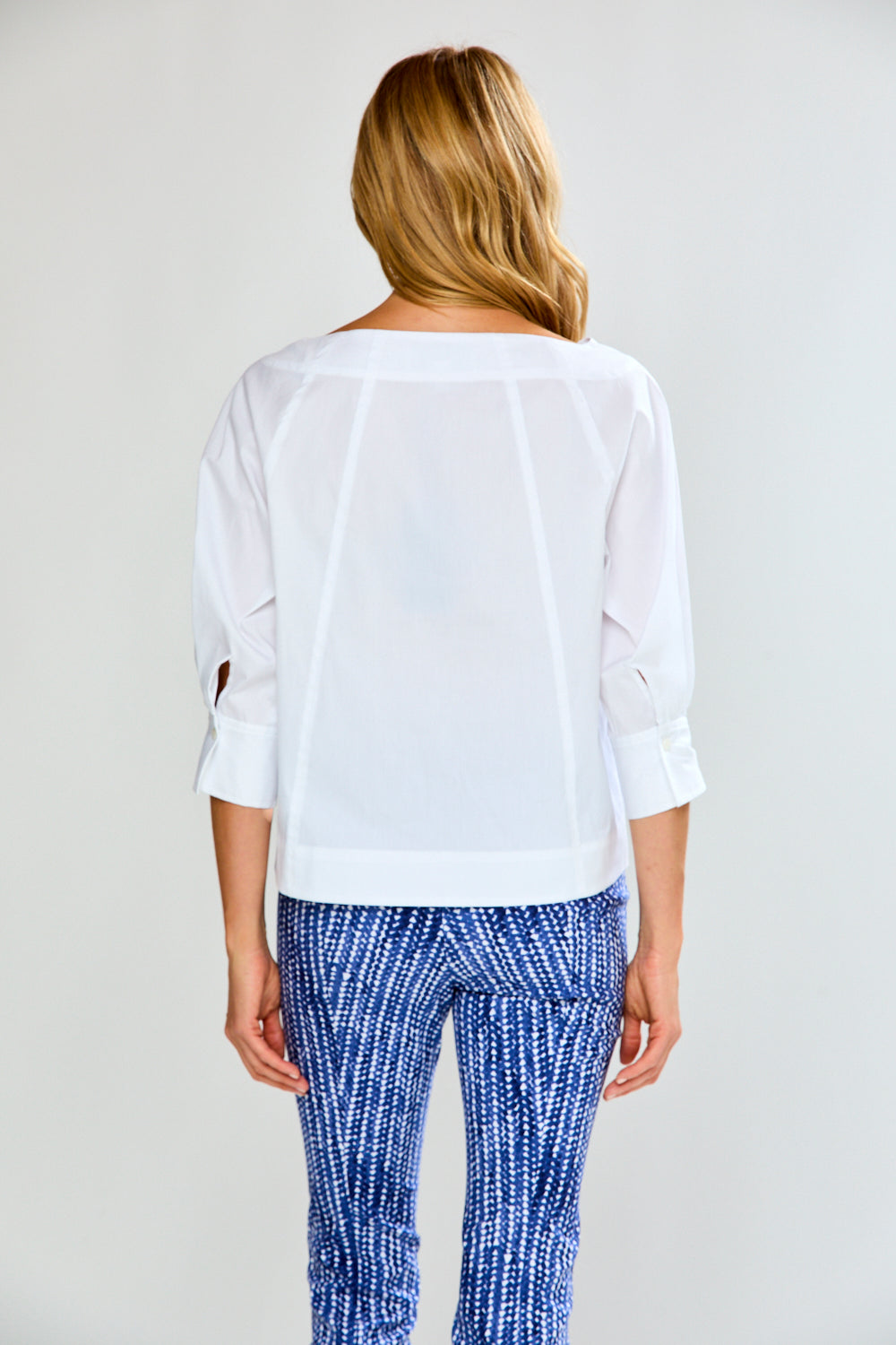 Woman wearing a white blouse and blue patterned pants on a plain background