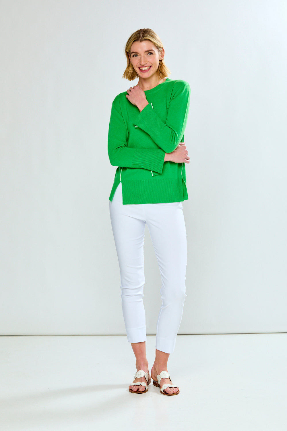 Woman wearing a green top and white pants against a white background
