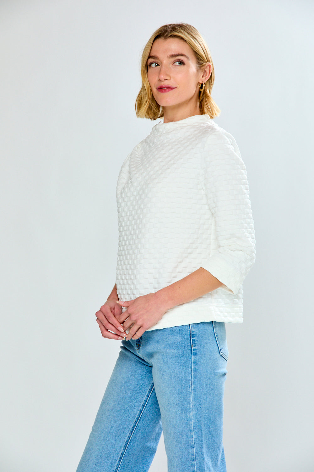 Woman wearing a white textured sweater and light blue jeans on a plain background