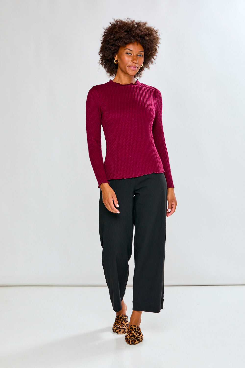 Woman wearing a burgundy shirt and black pants on a white background