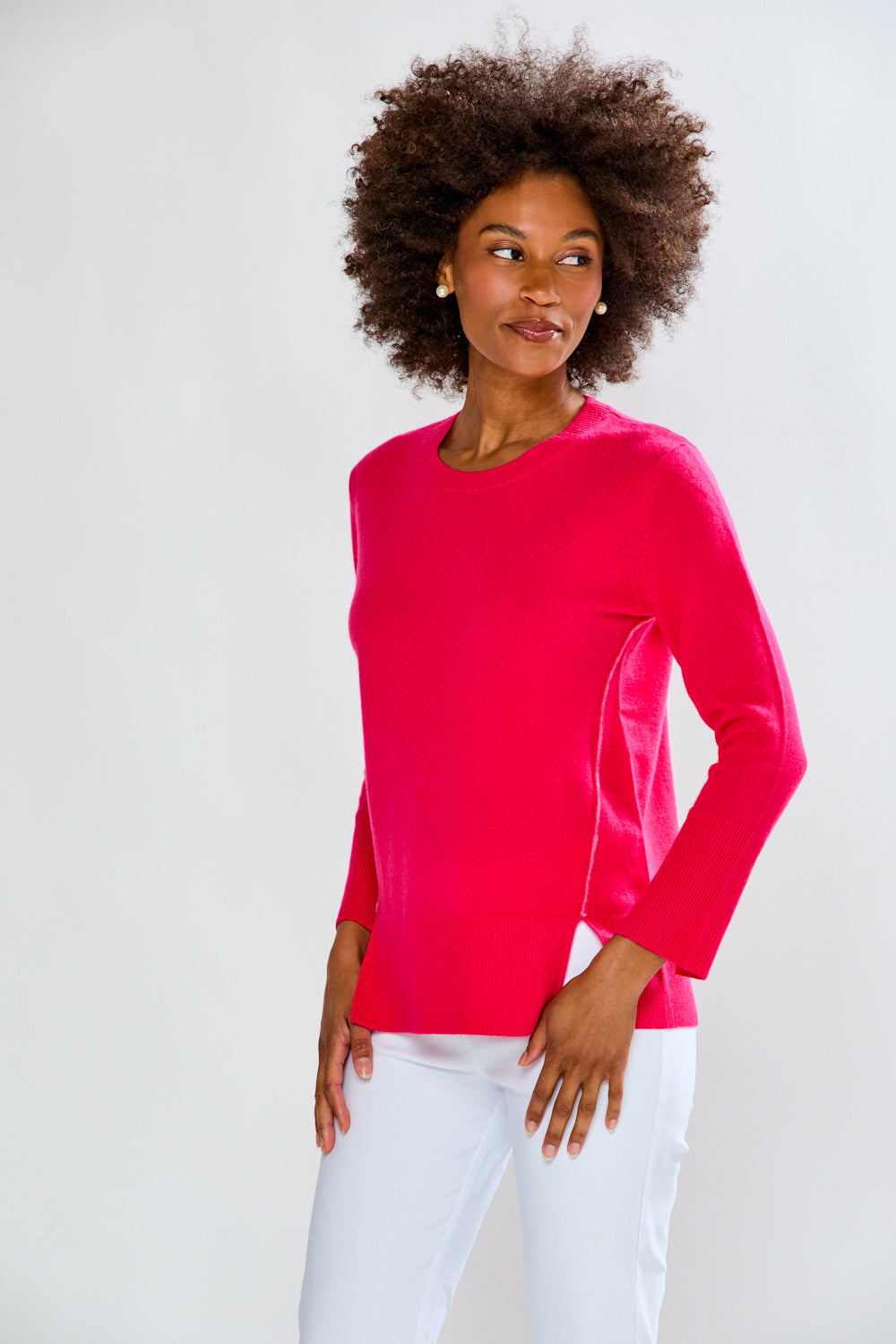 Woman wearing a bright pink long-sleeve top and white pants against a plain background