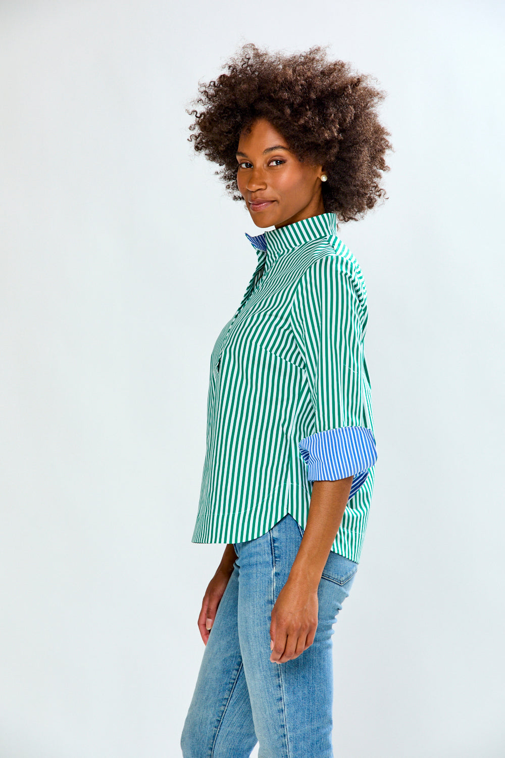 Woman wearing a green and white striped shirt with rolled-up sleeves and blue jeans on a white background
