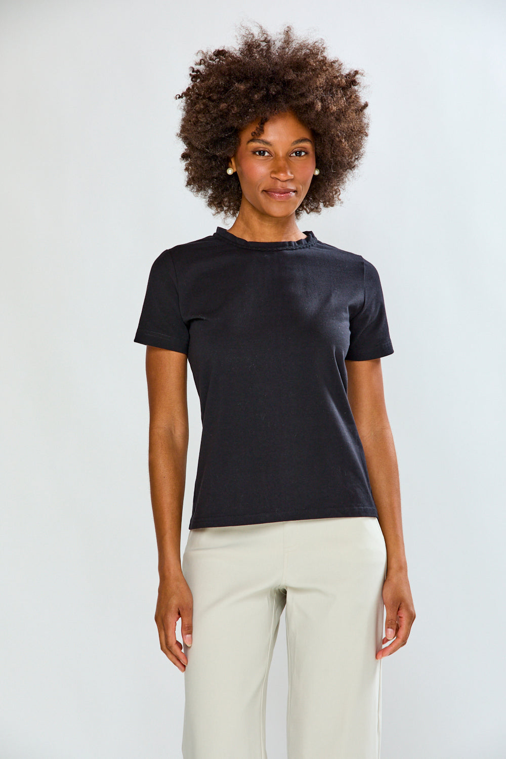 Woman wearing a black t-shirt and white pants against a plain background