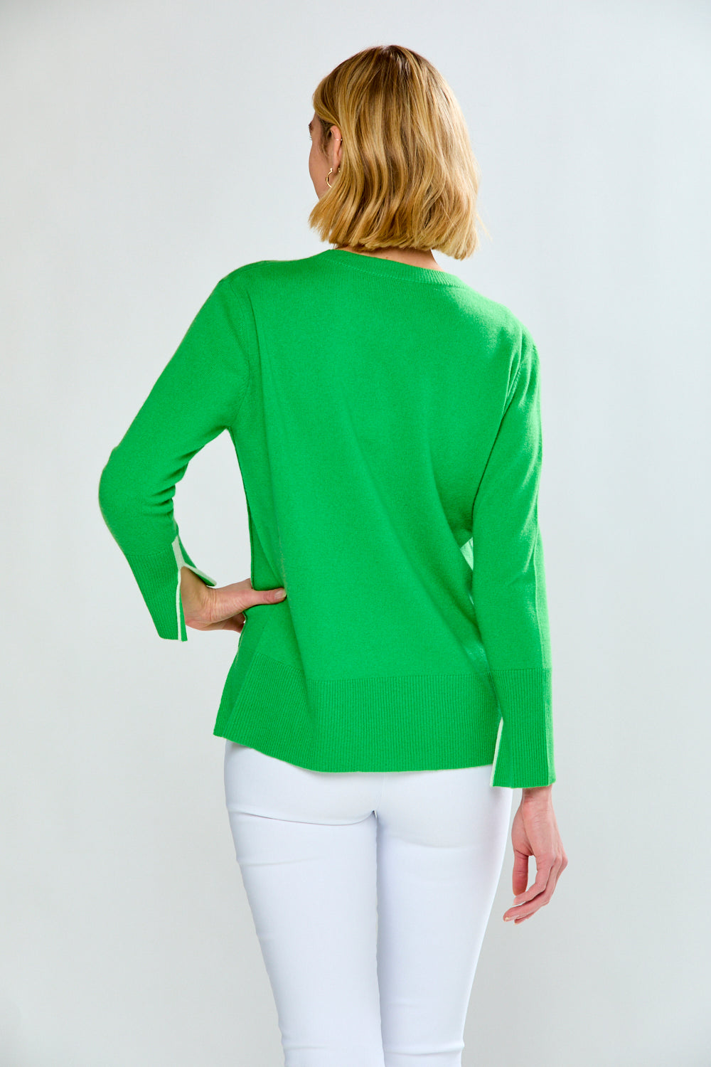 Woman wearing a green sweater and white pants on a plain background