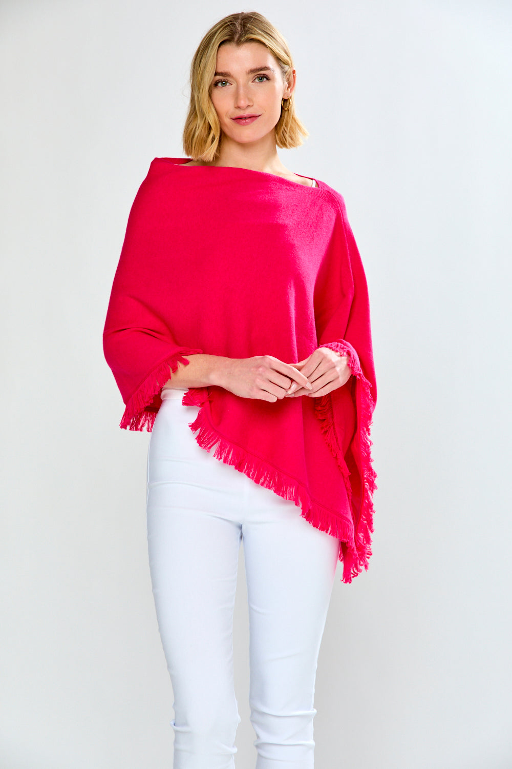 Woman wearing a bright pink poncho over a white top and pants on a white background