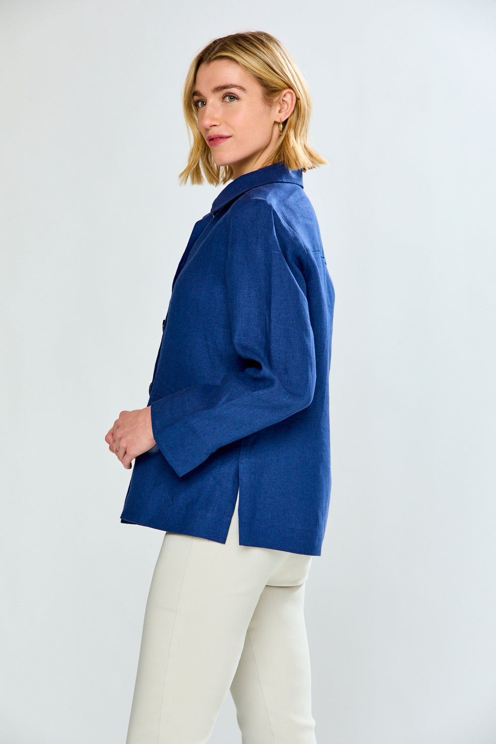 Woman wearing a blue jacket and white pants on a light gray background