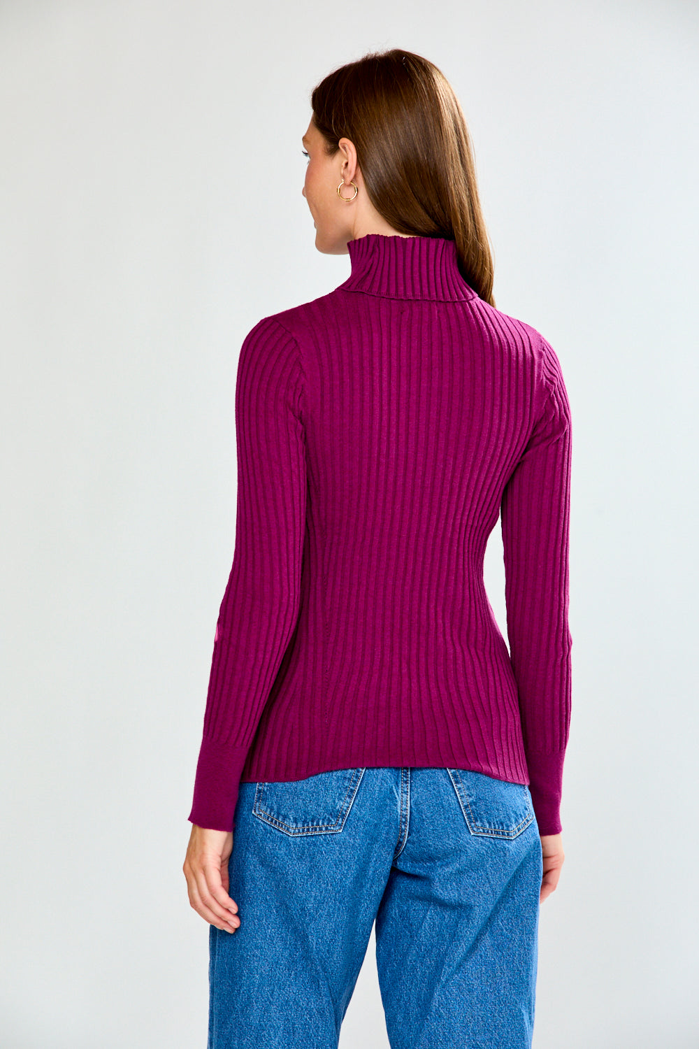 Woman wearing a maroon ribbed turtleneck sweater and blue jeans on a white background