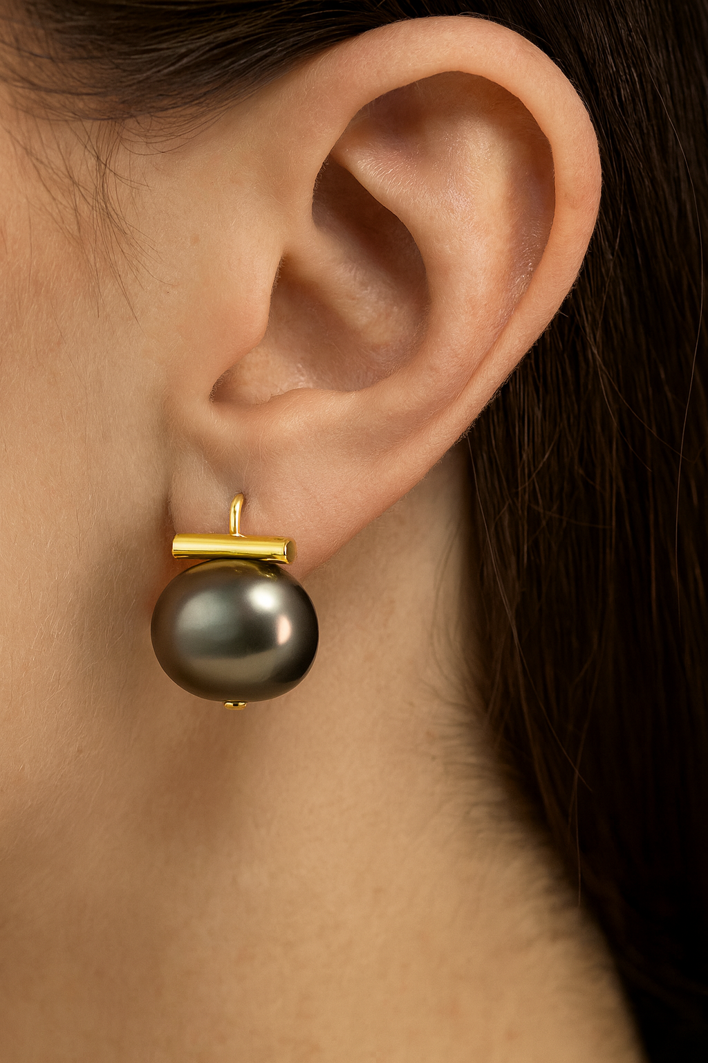 Close-up of an ear wearing a black pearl earring with gold setting.