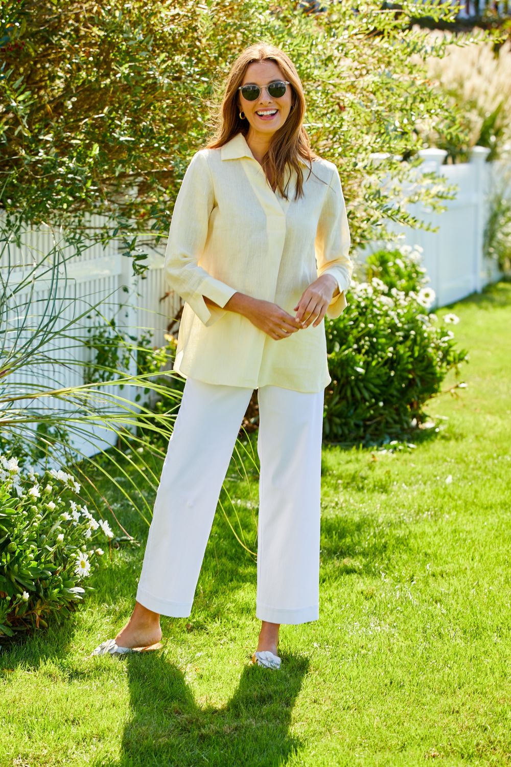 Woman wearing white pants and a yellow linen blouse in a garden