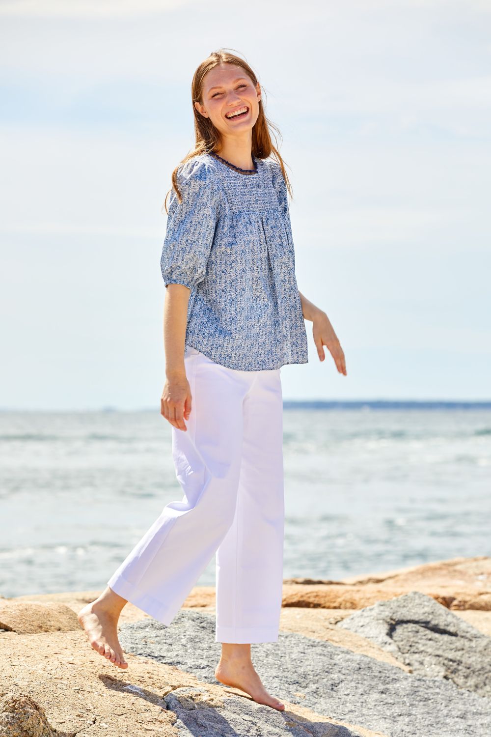 Woman on beach rocks wearing white pants and a blue blouse