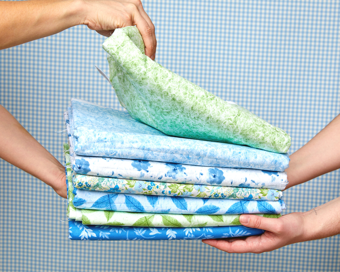 Two hands holding a pile of different green and blue fabric.