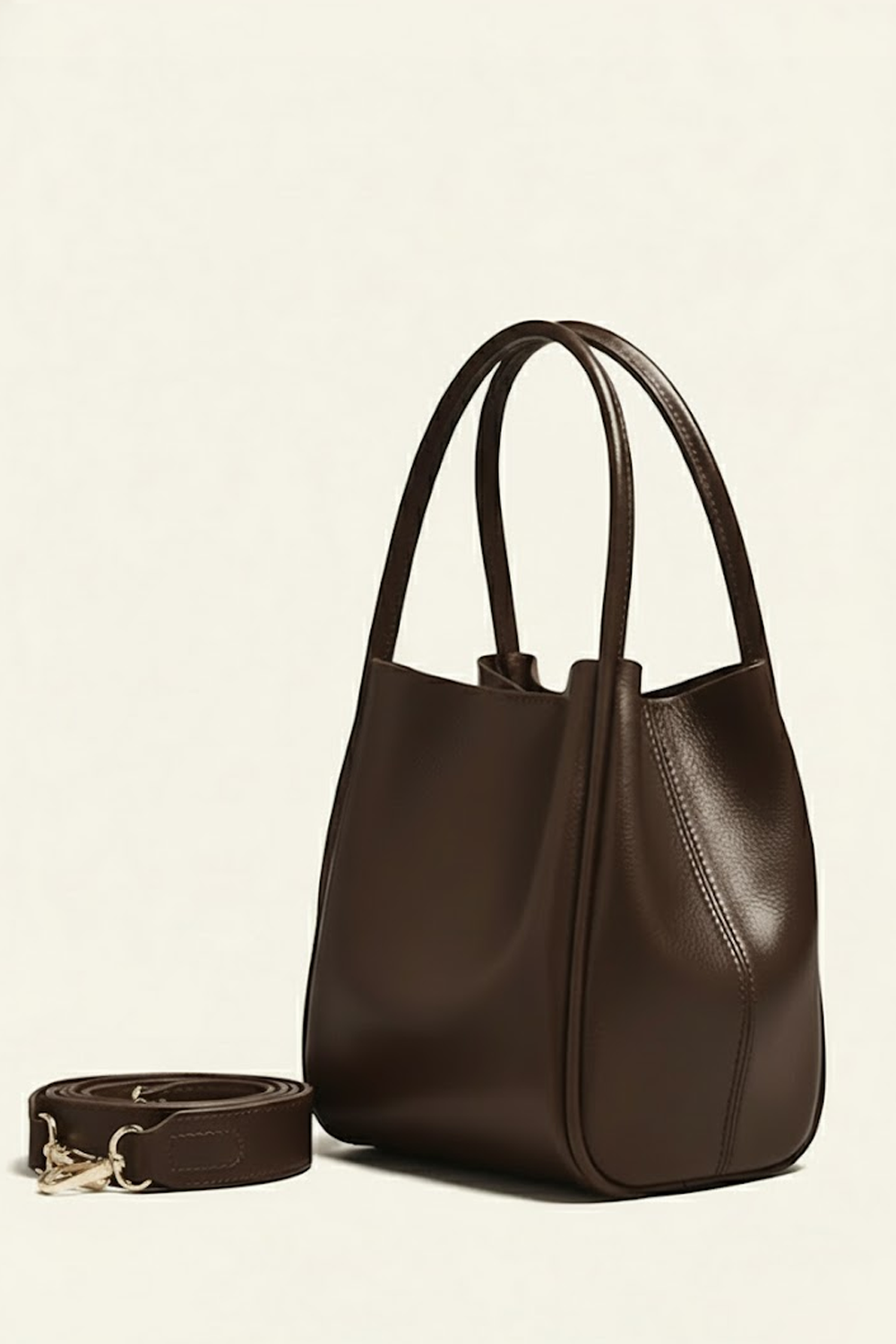 Brown leather handbag with matching strap on a beige background