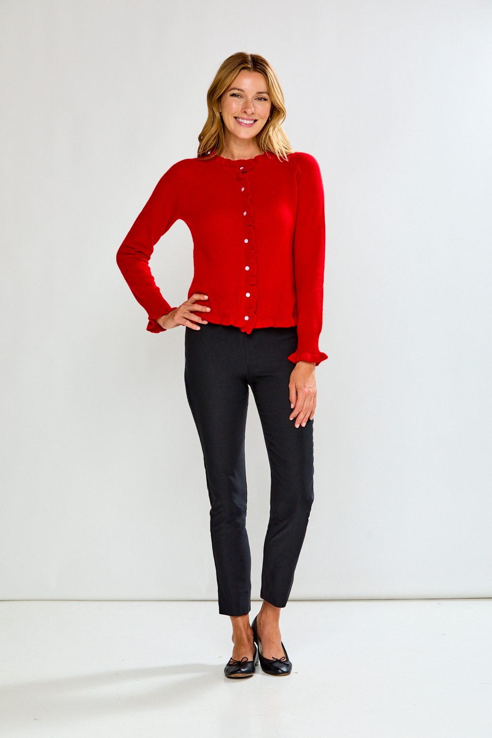 Woman wearing a red cardigan and black pants against a white background