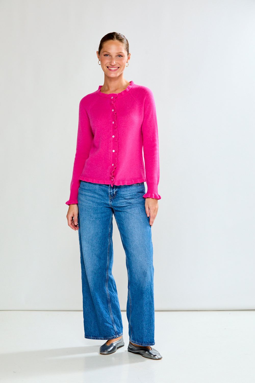 Woman wearing a Fuchsia cardigan and blue jeans on a white background