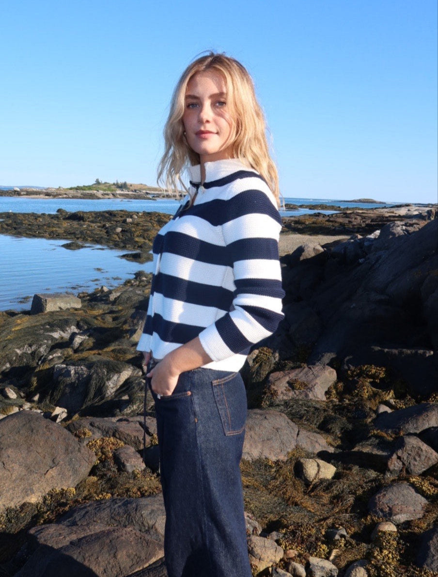 Woman in a striped sweater and jeans standing on rocks by the water