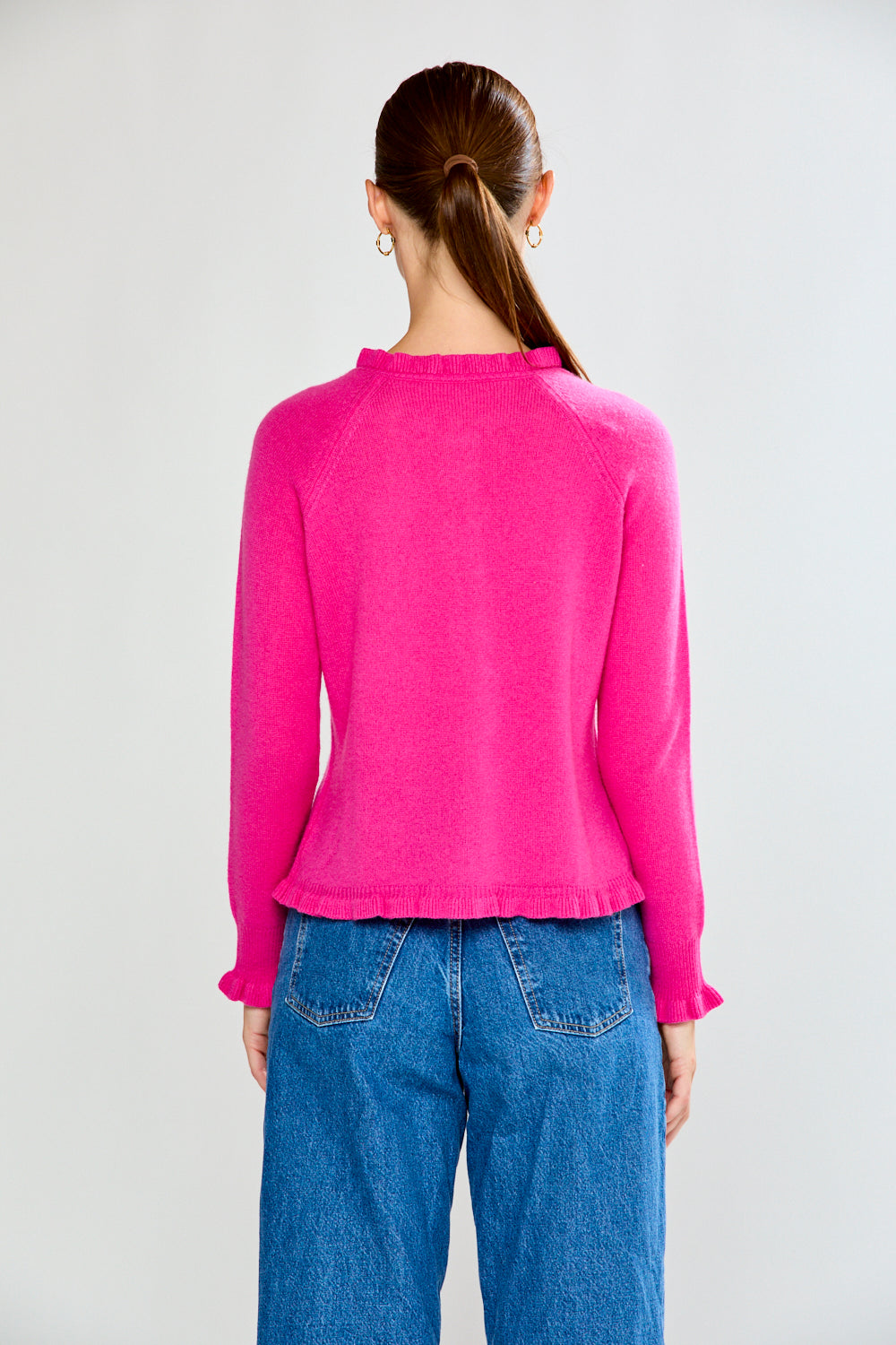 Woman wearing a Fuchsia cardigan and blue jeans on a white background