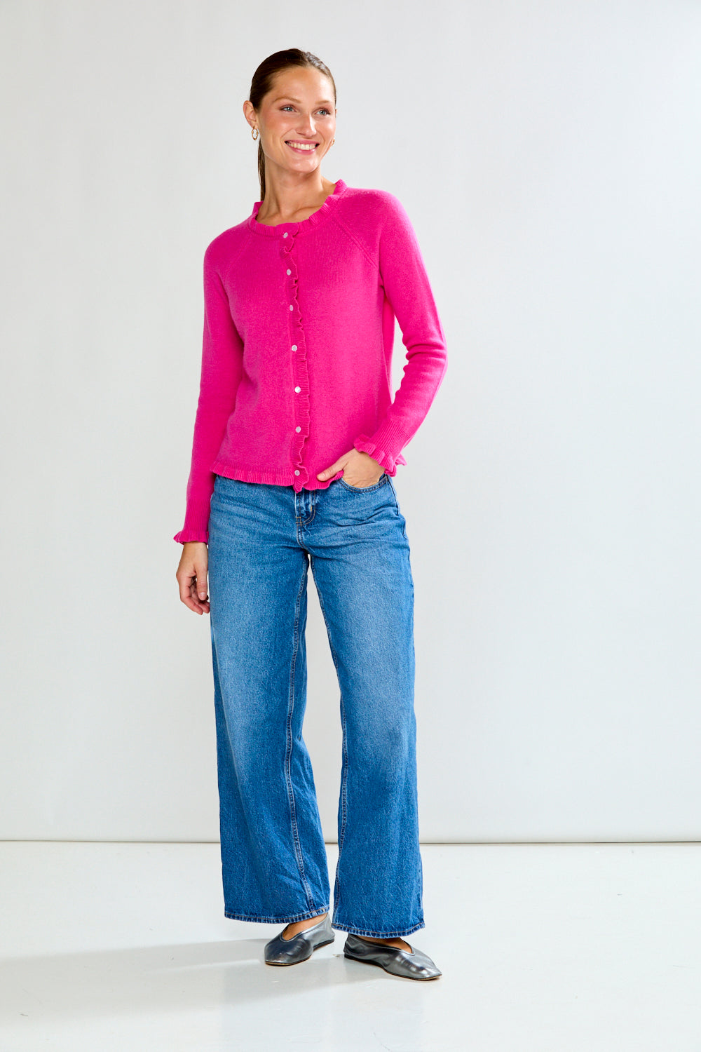 Woman wearing a Fuchsia cardigan and blue jeans on a white background