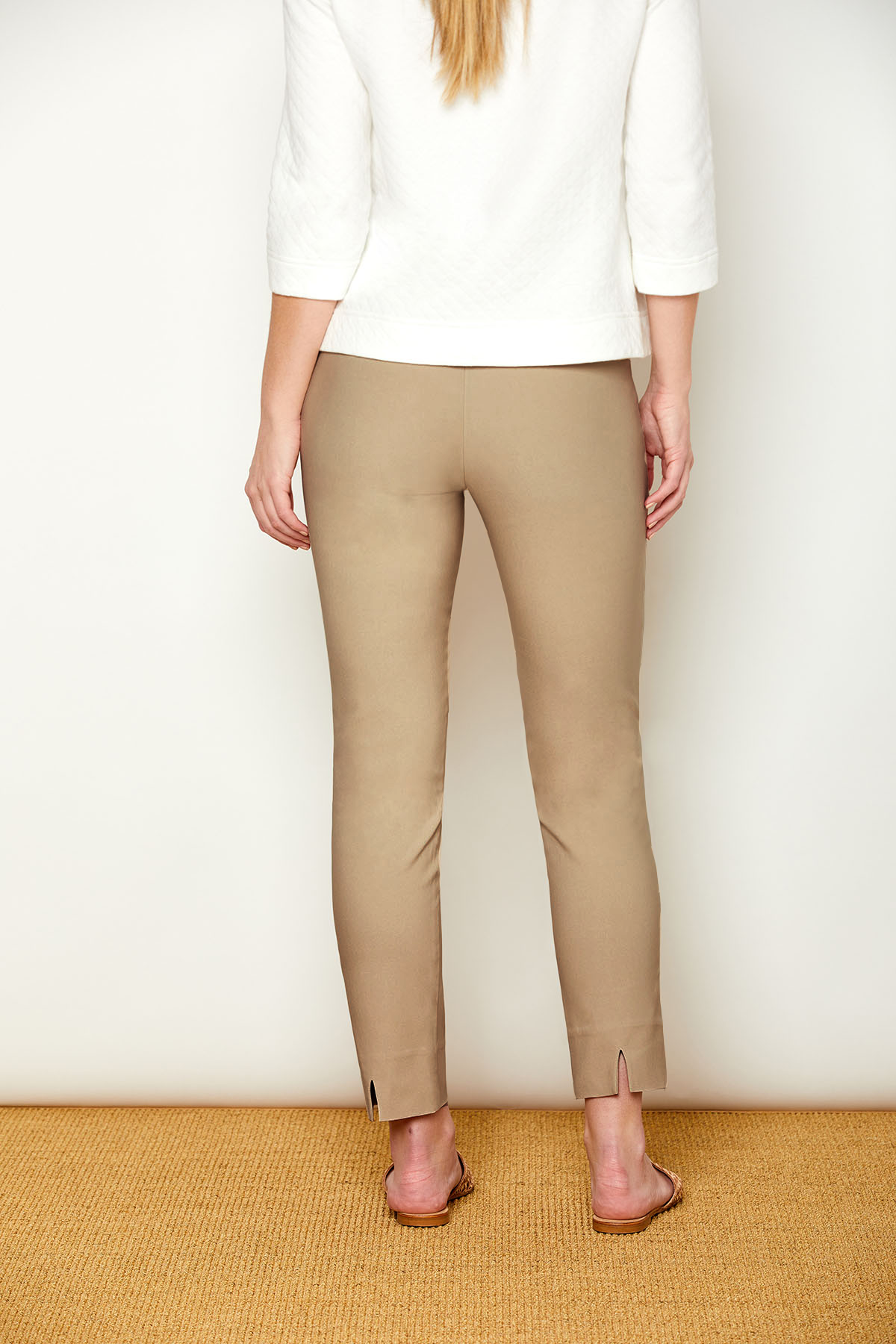 Person wearing beige pants and a white top against a plain background