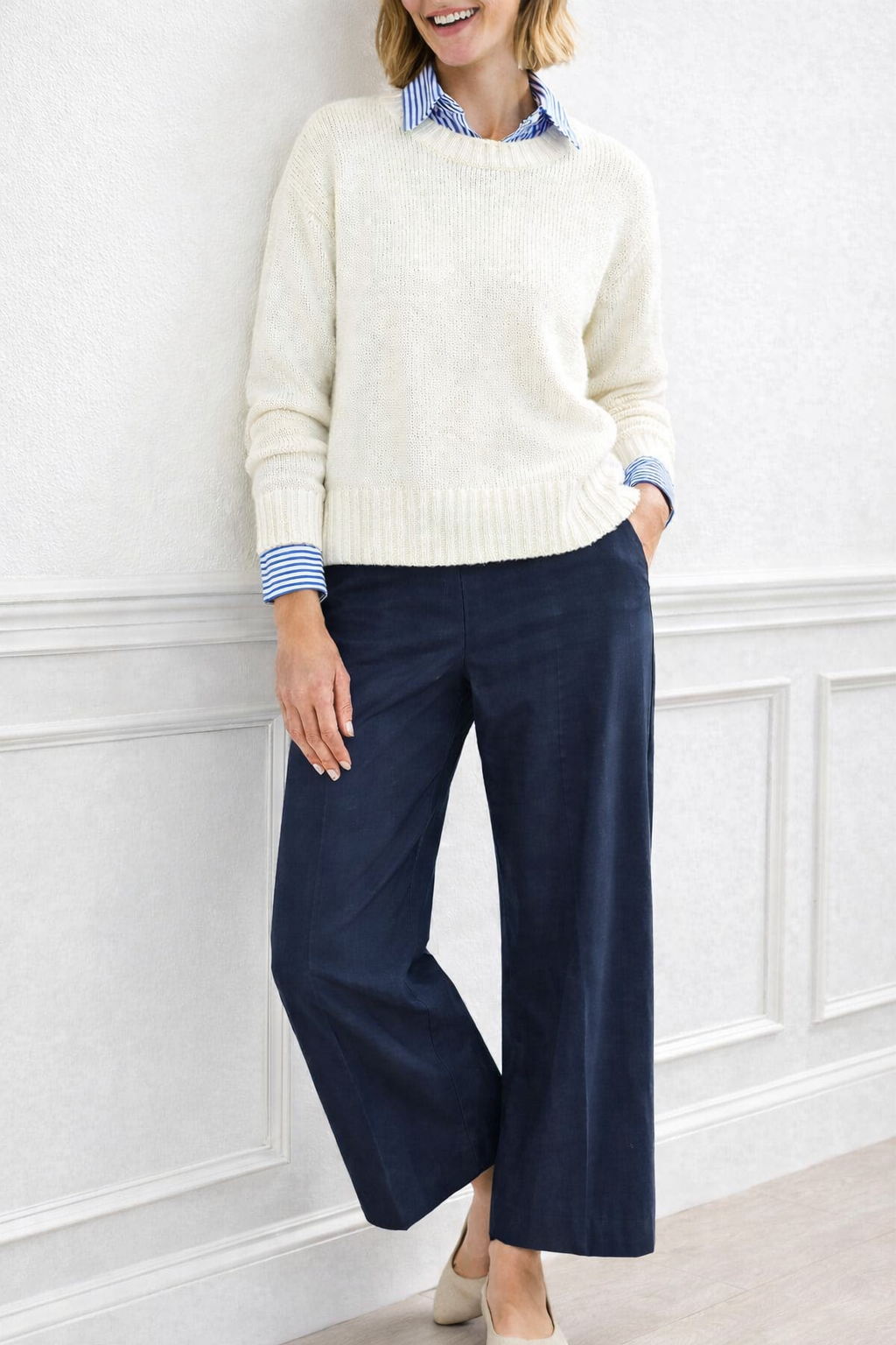 Woman wearing navy pants, an ivory sweater, and a blue stripe blouse underneath