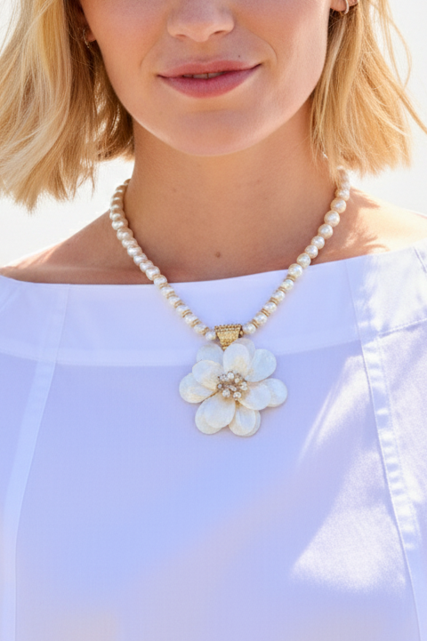 Pearl necklace with a floral pendant worn by a person against a white background