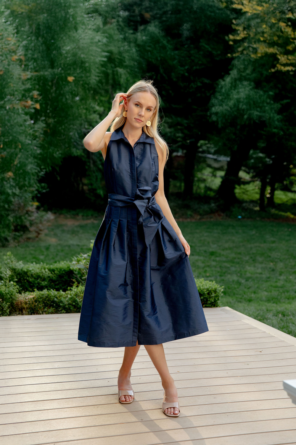 Woman in a navy dress standing on a wooden deck with greenery in the background