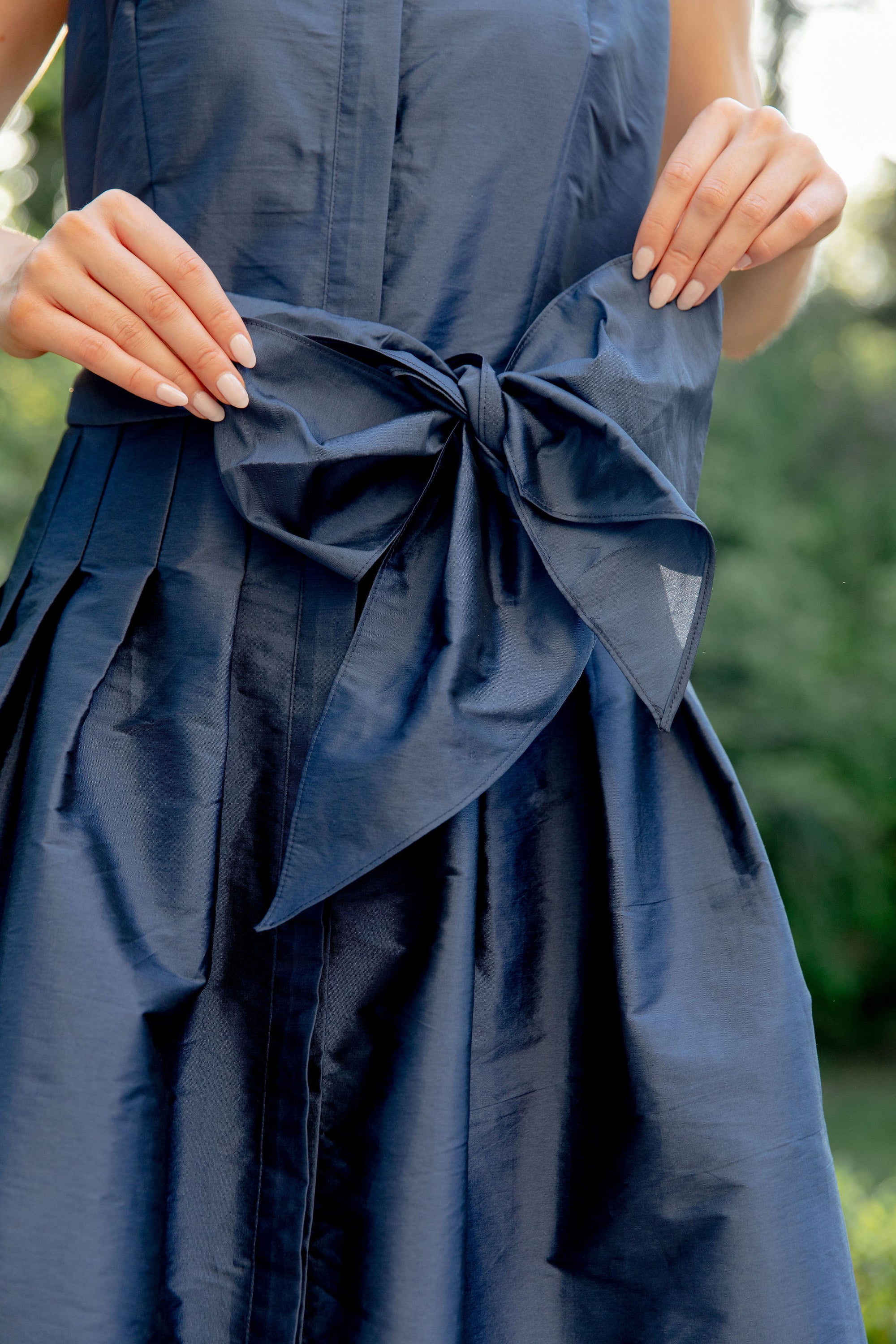 Navy blue dress with a large bow detail on a blurred natural background