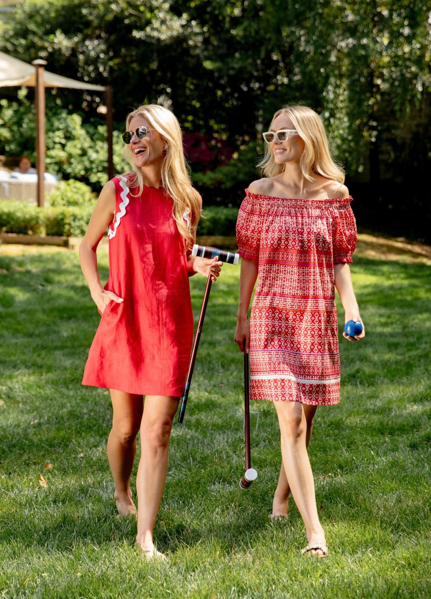 Two women walking side by side in red dresses playing croquet