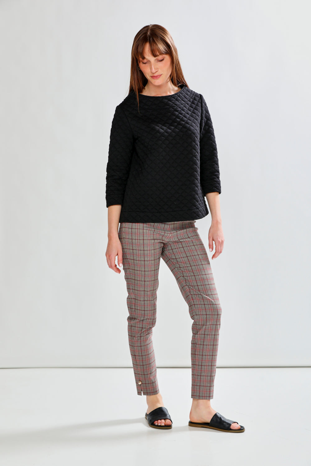 Woman wearing a black quilted pullover and plaid pants on a white background