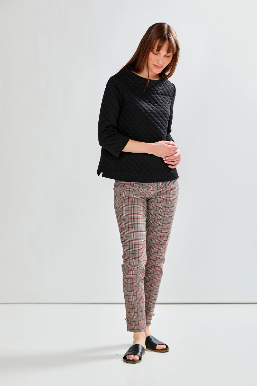 Woman wearing a black quilted top and plaid pants on a white background
