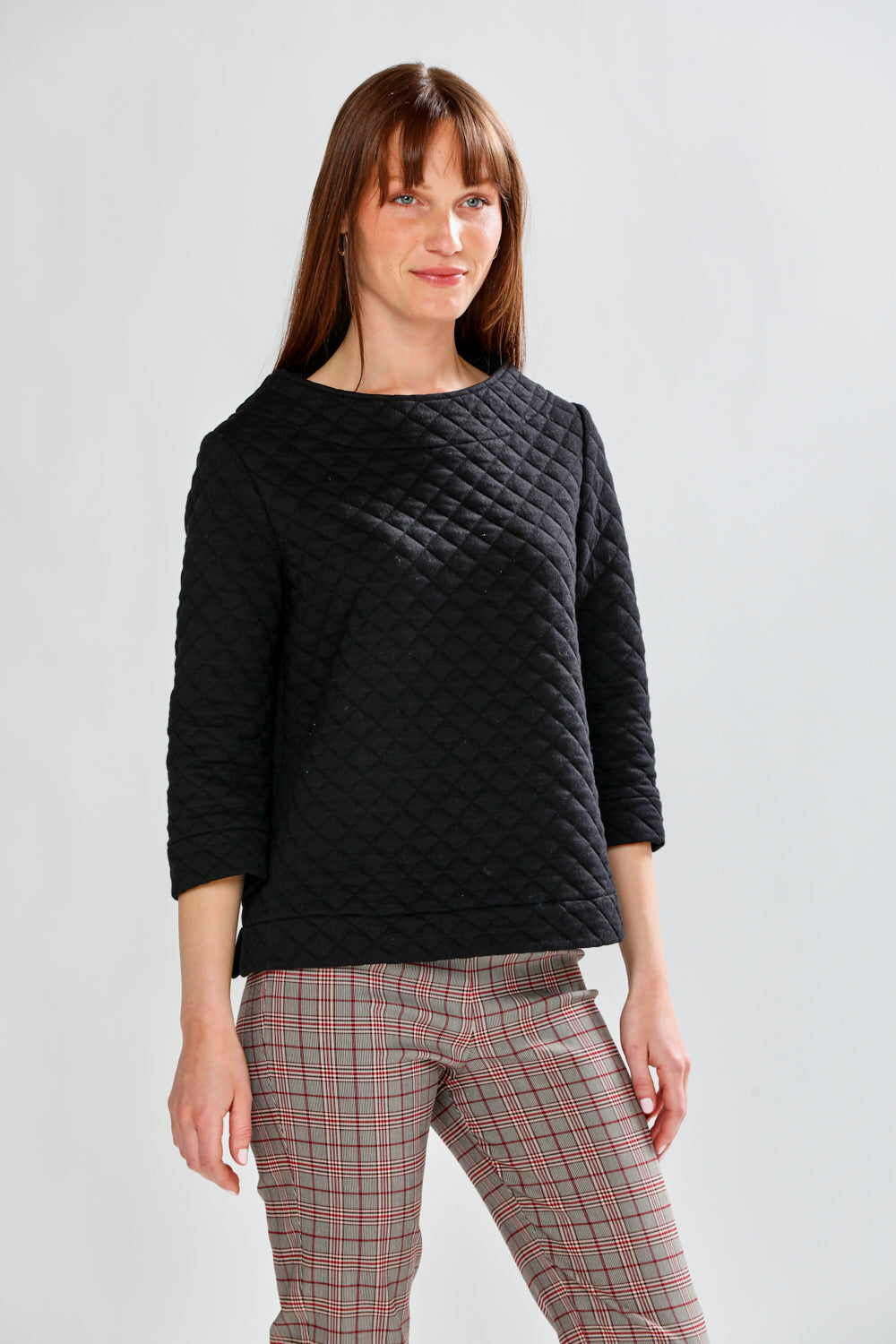 Woman wearing a black quilted sweater and plaid pants on a white background