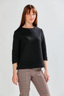 Woman wearing a black quilted sweater and plaid pants on a white background