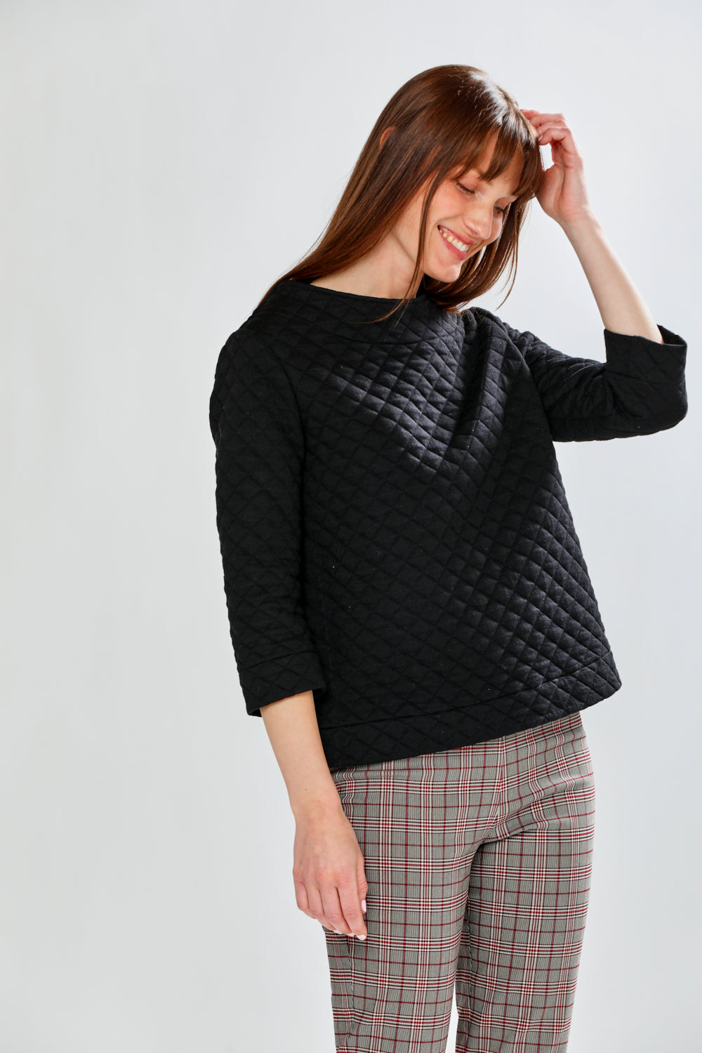 Woman wearing a black quilted sweater and plaid pants on a white background