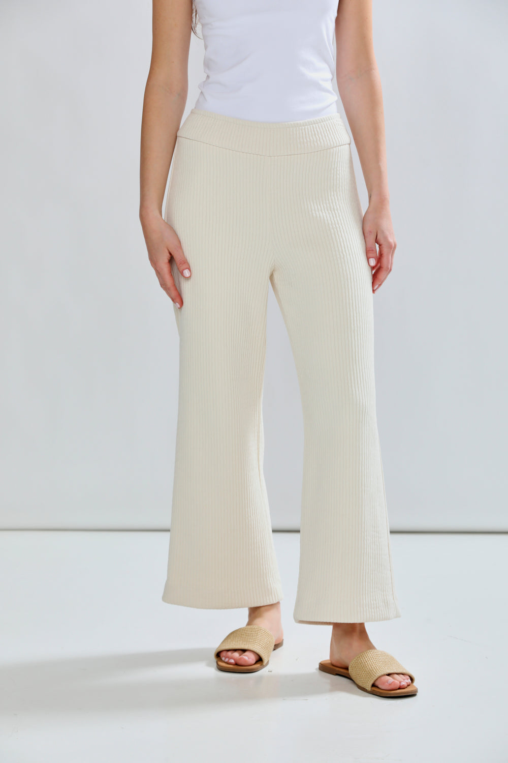 Person wearing beige wide-leg pants and a white top on a plain background