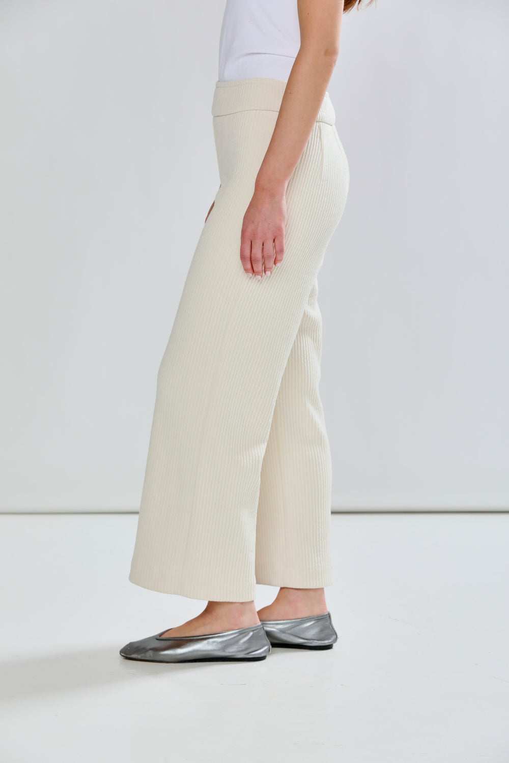 Person wearing cream wide-leg pants and silver flats on a white background