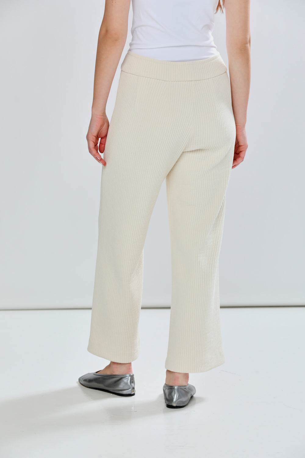 Person wearing light-colored pants and a white top on a plain background