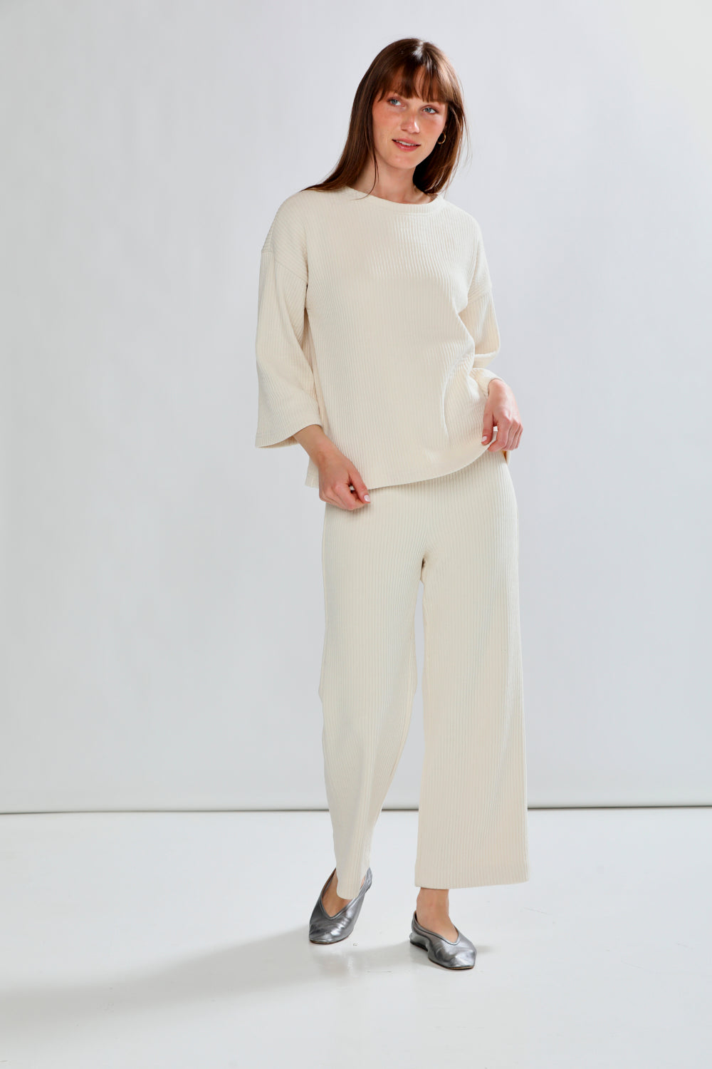 Woman wearing a cream outfit with wide-leg pants against a white background