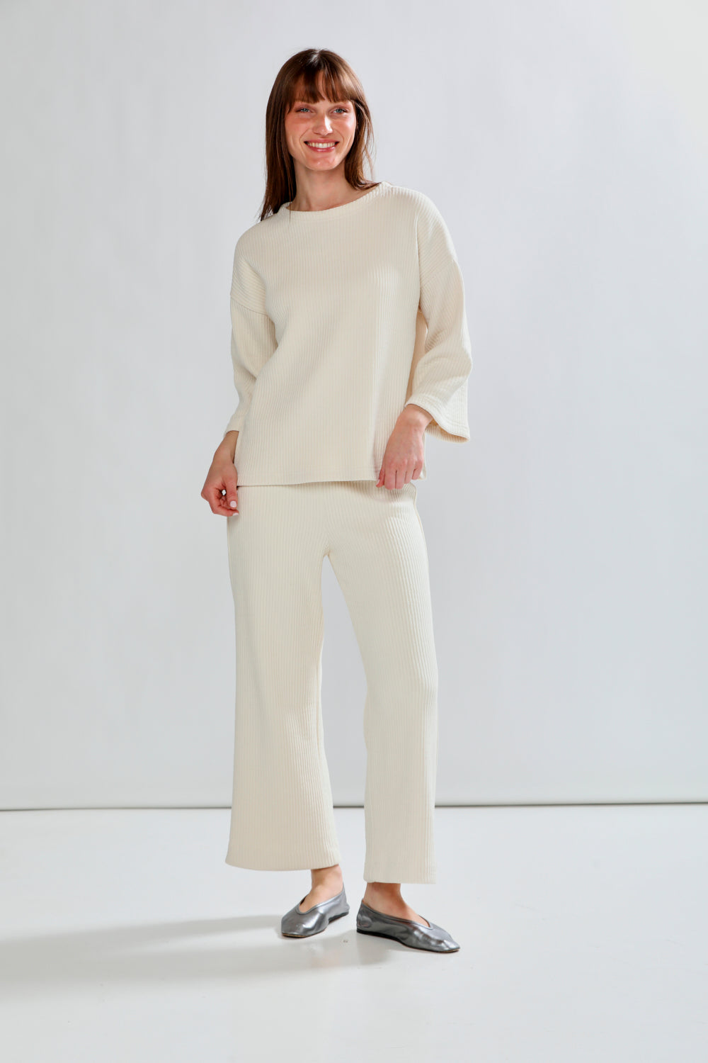 Woman wearing a cream sweater and pants against a white background
