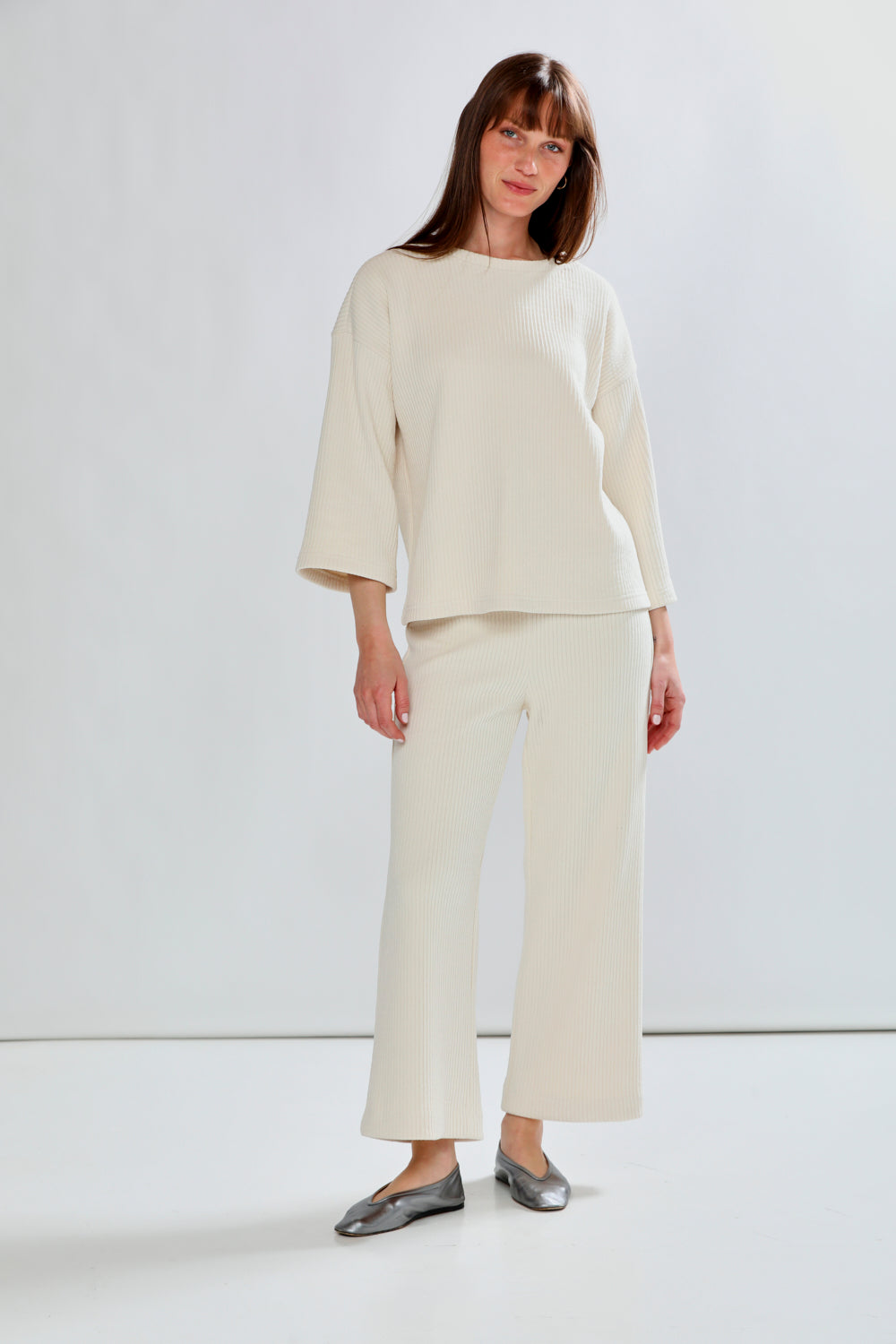 Woman wearing a beige outfit with wide-leg pants against a white background
