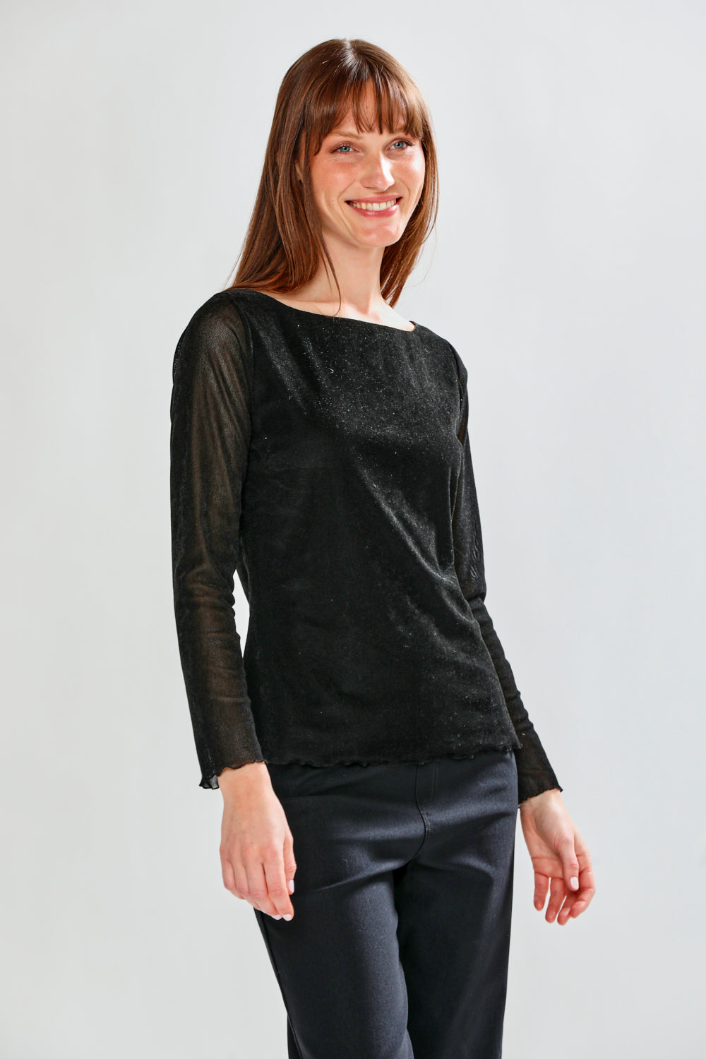 Woman wearing a black long-sleeve top and dark pants on a light gray background