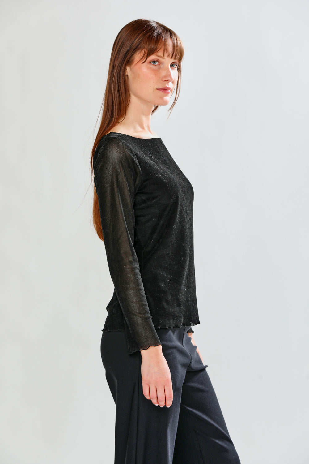 Woman wearing a black long-sleeve top and dark pants on a light gray background