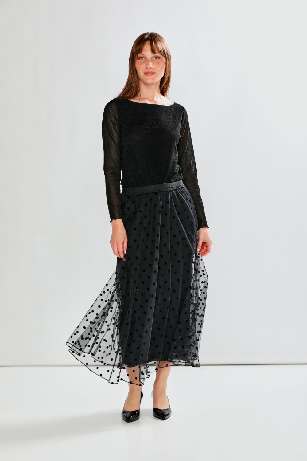 Person wearing a black polka dot tulle skirt with a plain background