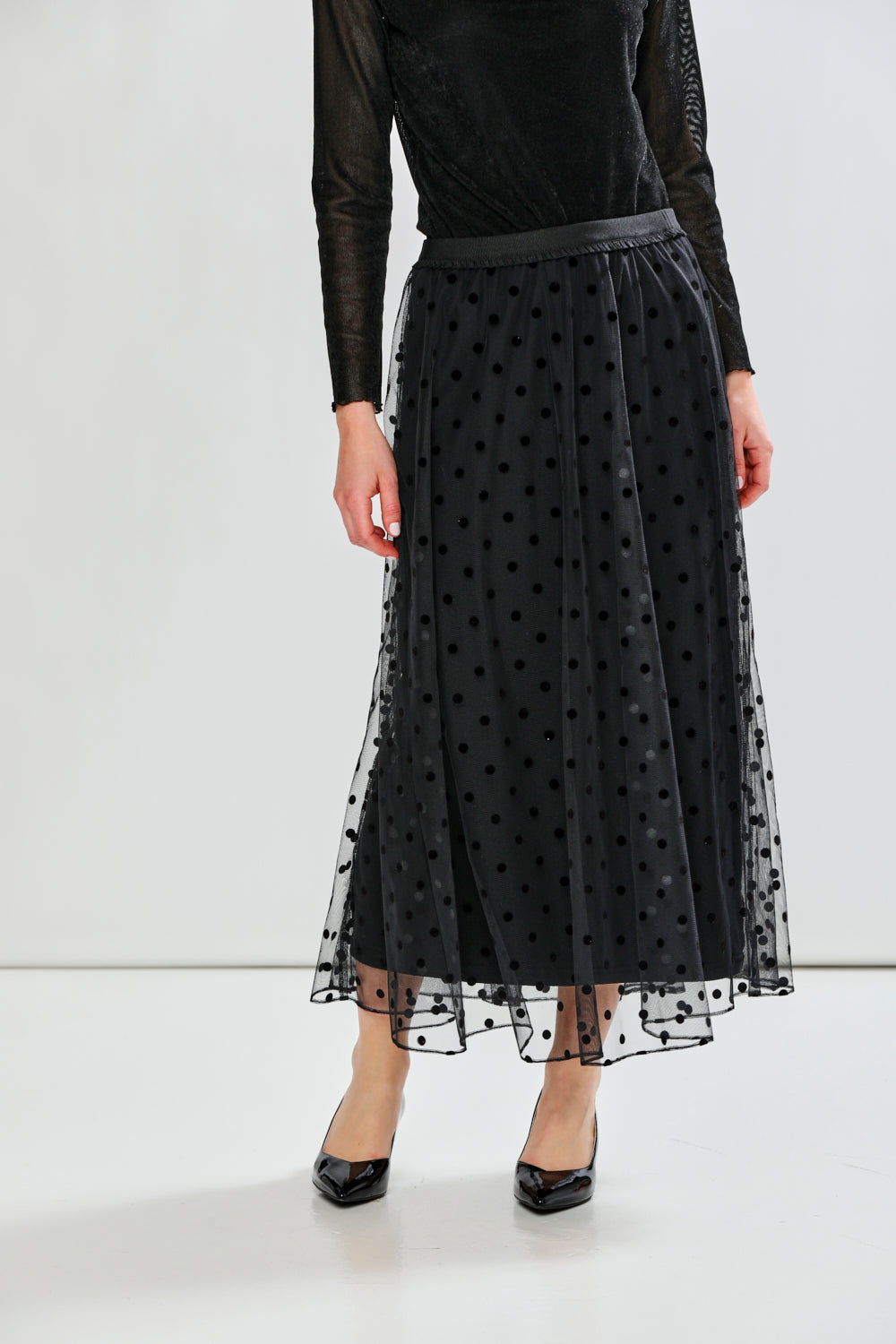 Person wearing a black polka dot tulle skirt with a plain background