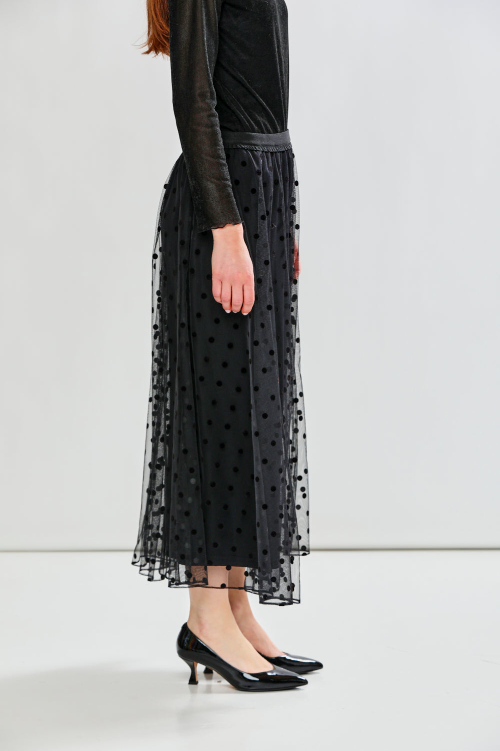 Person wearing a black polka dot tulle skirt with a plain background