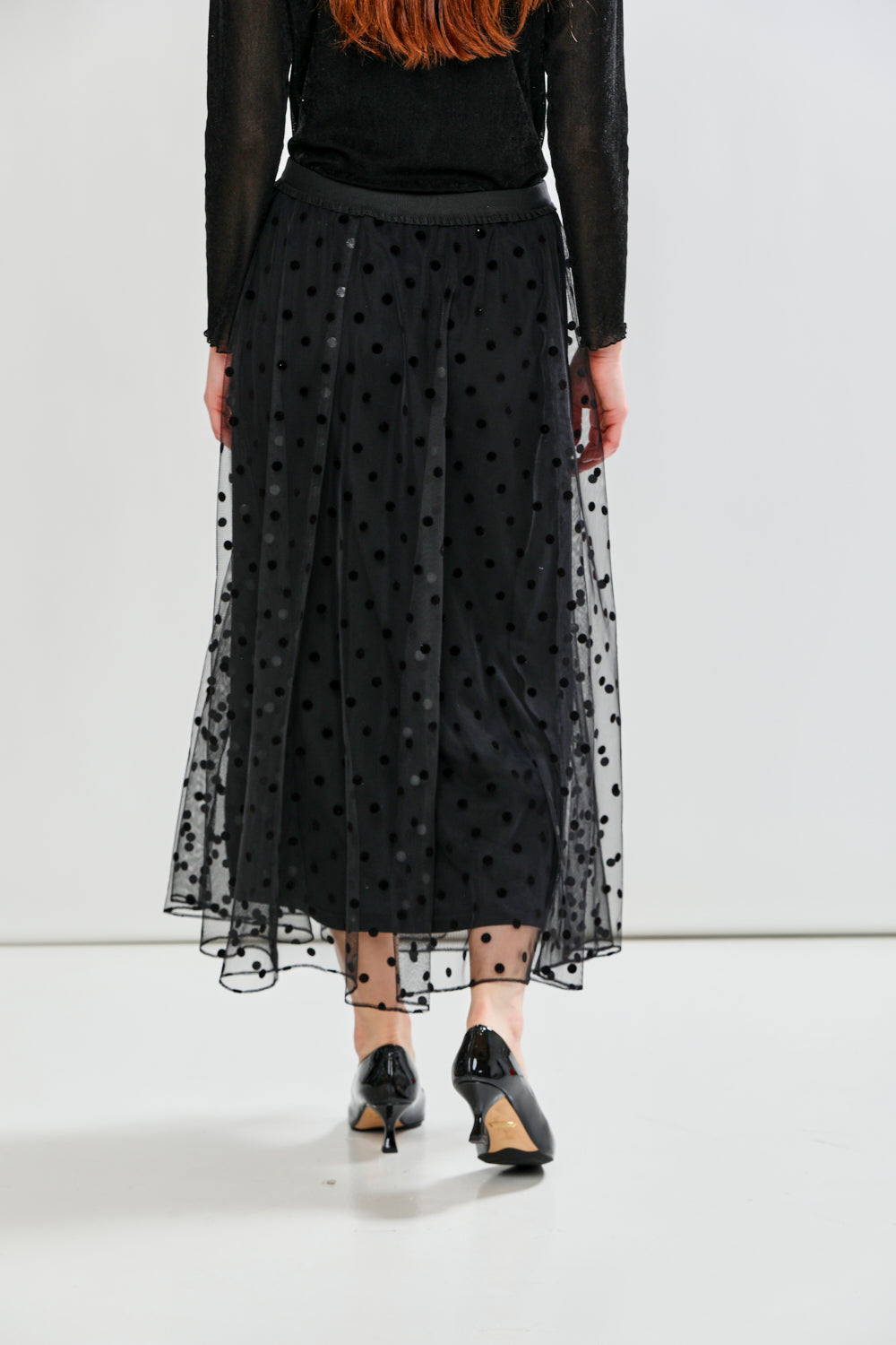 Person wearing a black polka dot tulle skirt with a plain background