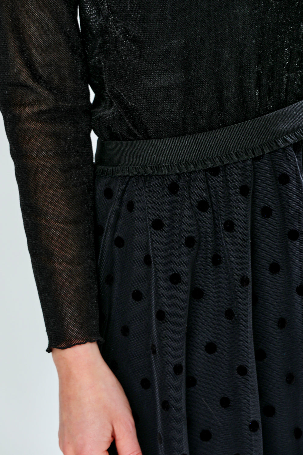 Person wearing a black polka dot tulle skirt with a plain background